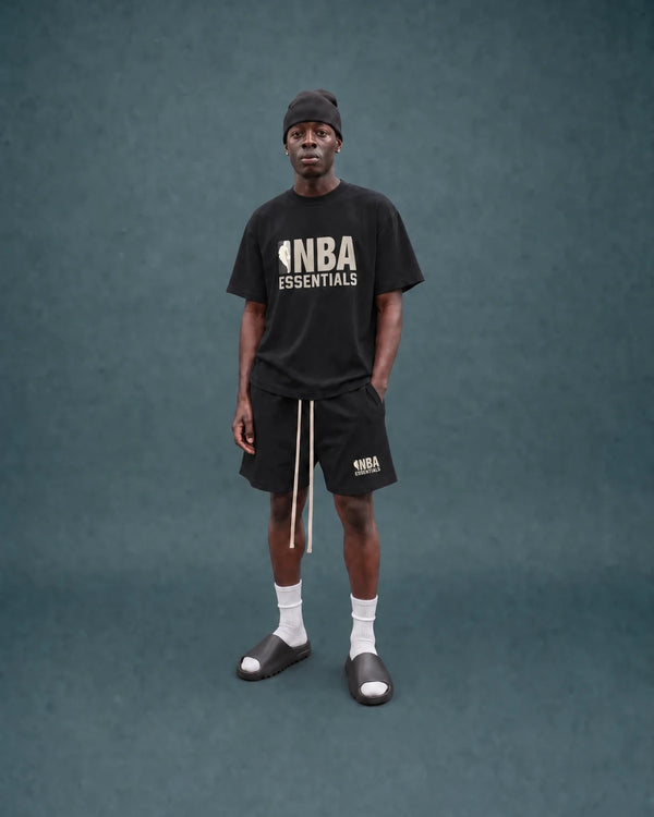 Model im NBA Essentials Shirt und Shorts vor blaugruenem Hintergrund