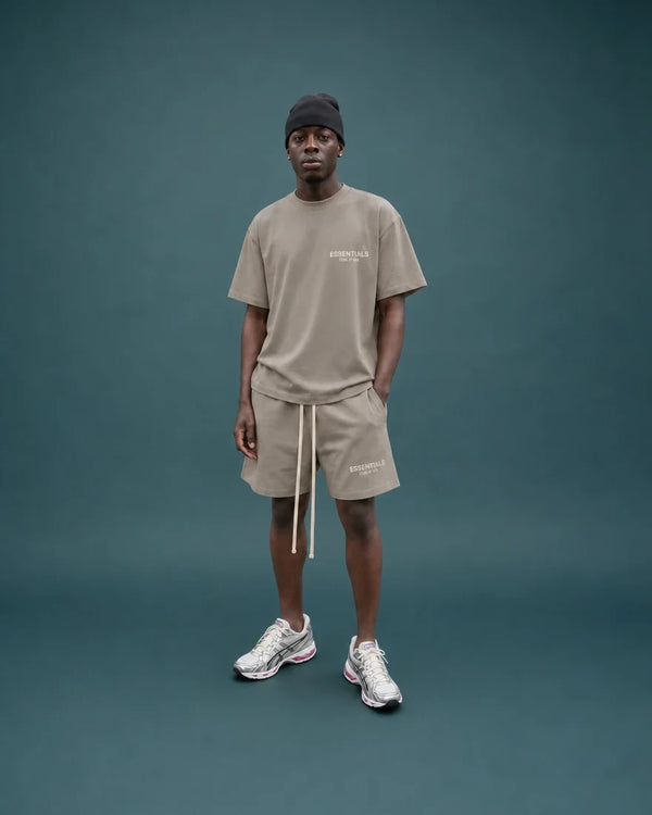 Model im Essentials Shirt und Shorts vor blaugruenem Hintergrund